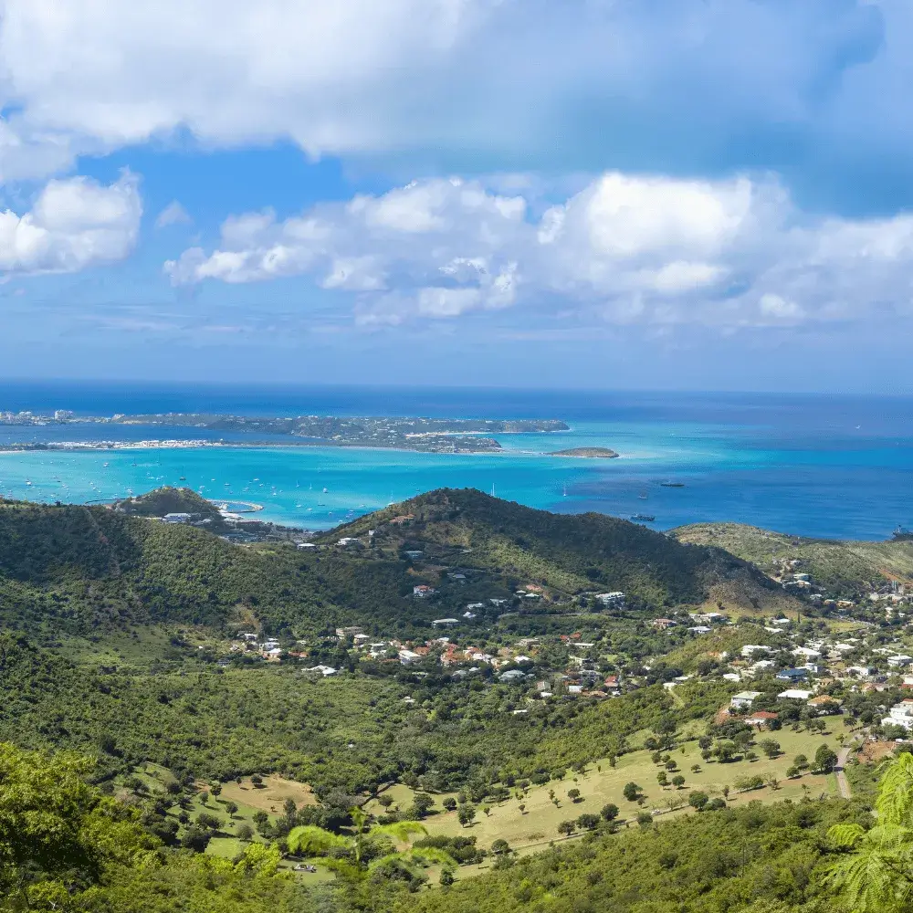 Panoramic view of green rolling hills leading down to the bright turquoise waters of Saint Martin island.