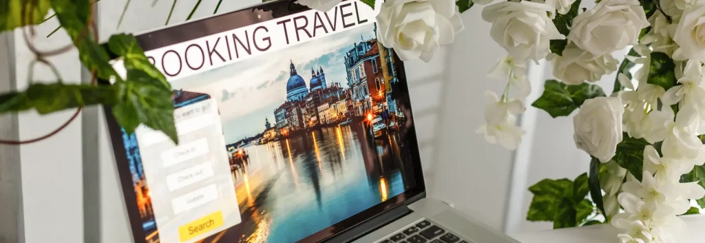 Laptop screen showing a European travel booking site with a view of Venice, framed by elegant white roses.
