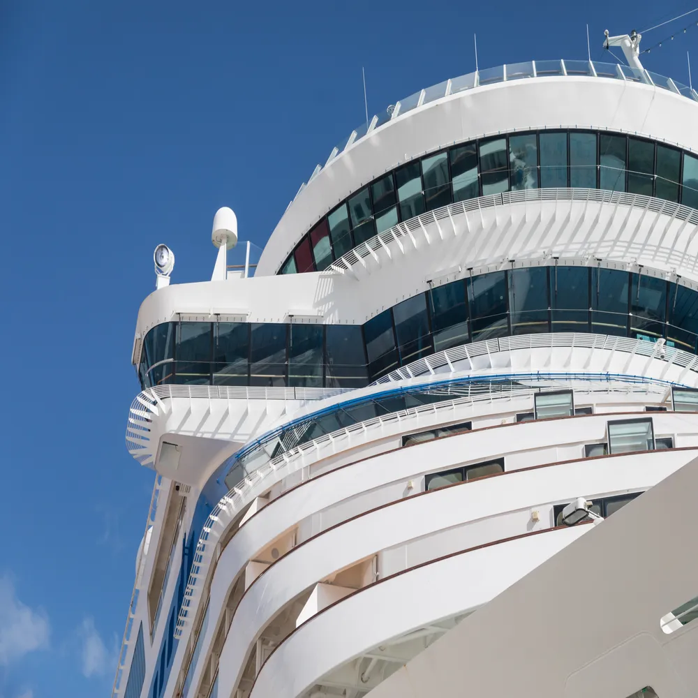 Close-up exterior view of a modern white luxury cruise ship's glass bridge and upper passenger decks gleaming against a clear blue sky.