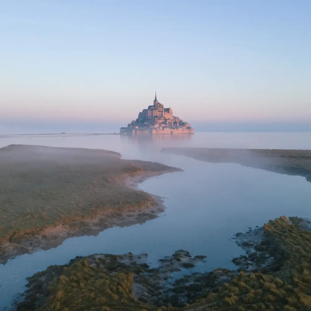 The breathtaking Mont Saint-Michel island commune rising out of the misty bay waters at dawn in France.