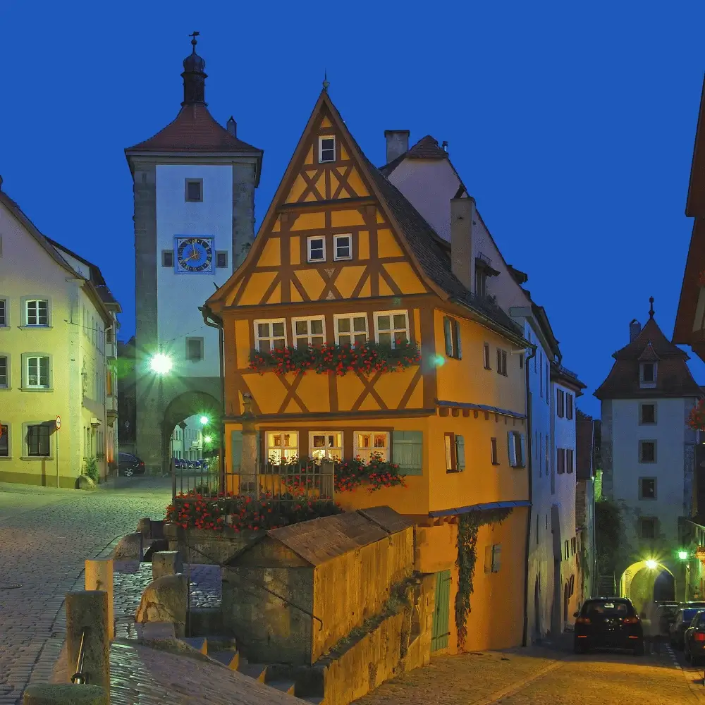 Charming medieval half-timbered houses and a clock tower illuminated at twilight in Rothenburg, Germany.