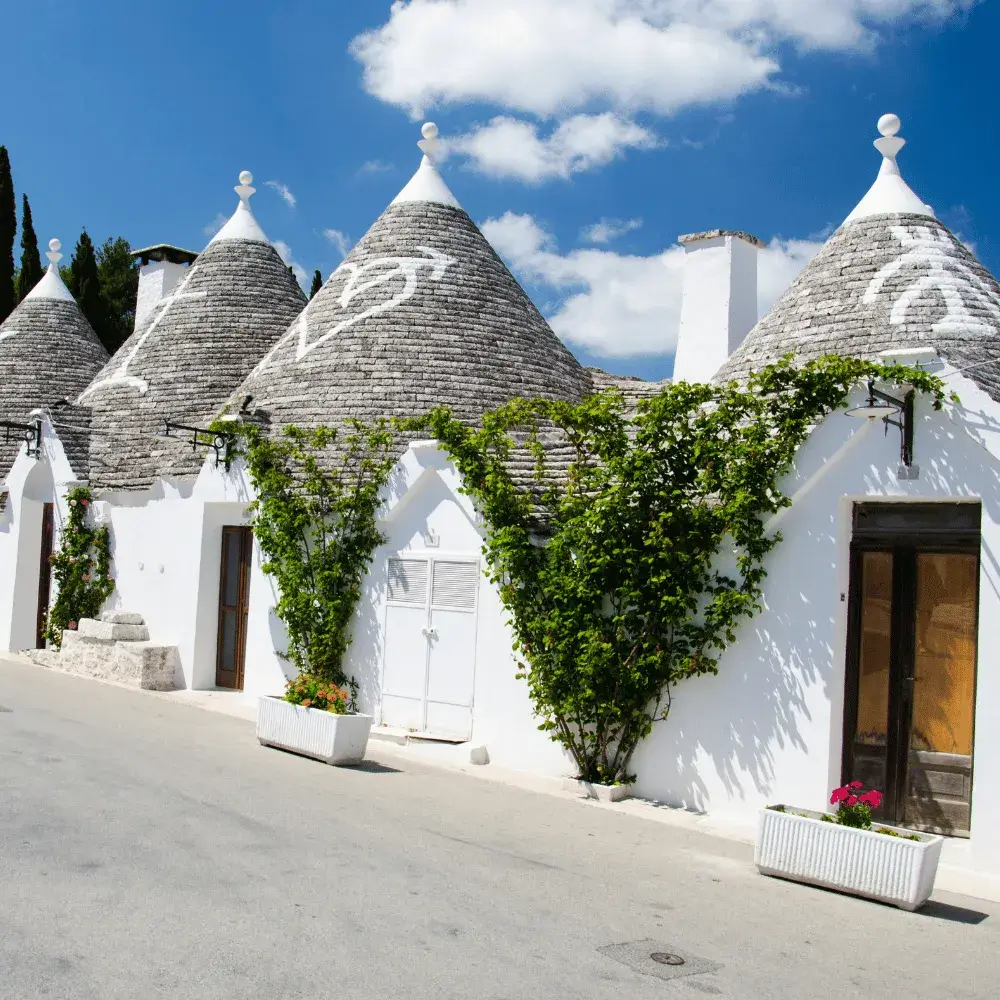 Unique whitewashed stone huts with conical roofs known as Trulli lining a sunny street in Alberobello, Italy.