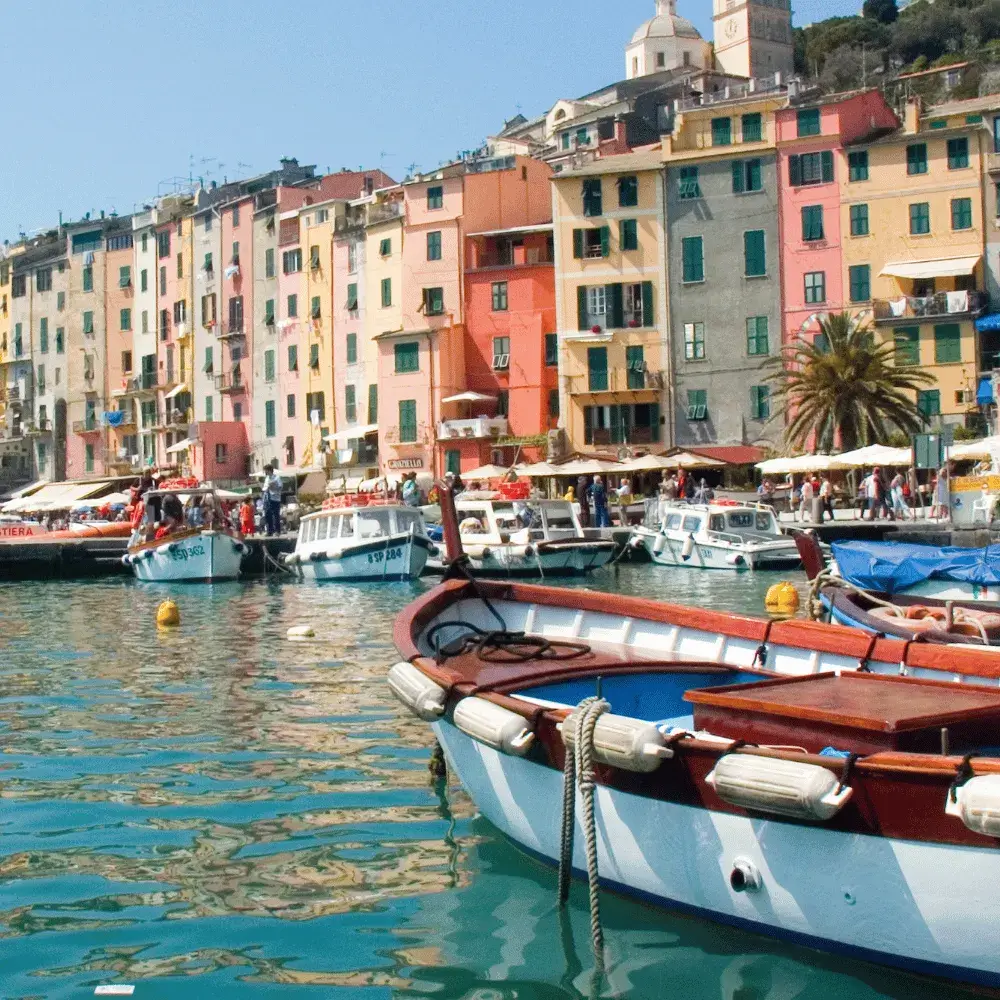 Vibrant pastel-colored buildings lining the bustling harbor filled with small wooden boats on the Italian Riviera.