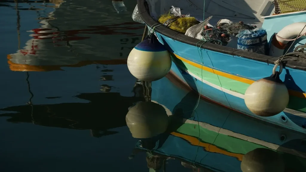 Close-up of a vibrant traditional Luzzu fishing boat floating in the clear waters of Marsaxlokk, Malta.