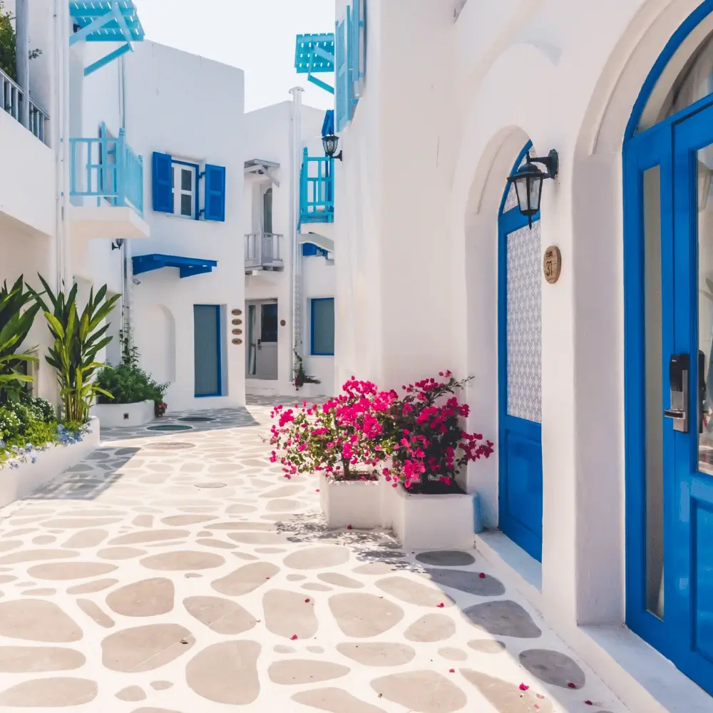 Classic bright white alleyways with vibrant blue doors, blue balconies, and pink flowers in Mykonos, Greece.