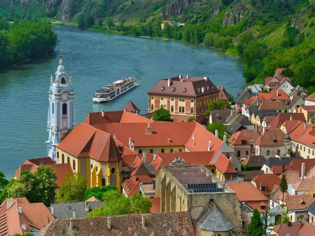 Aerial view of a river cruise ship sailing past the beautiful red-roofed buildings of Dürnstein, Austria.