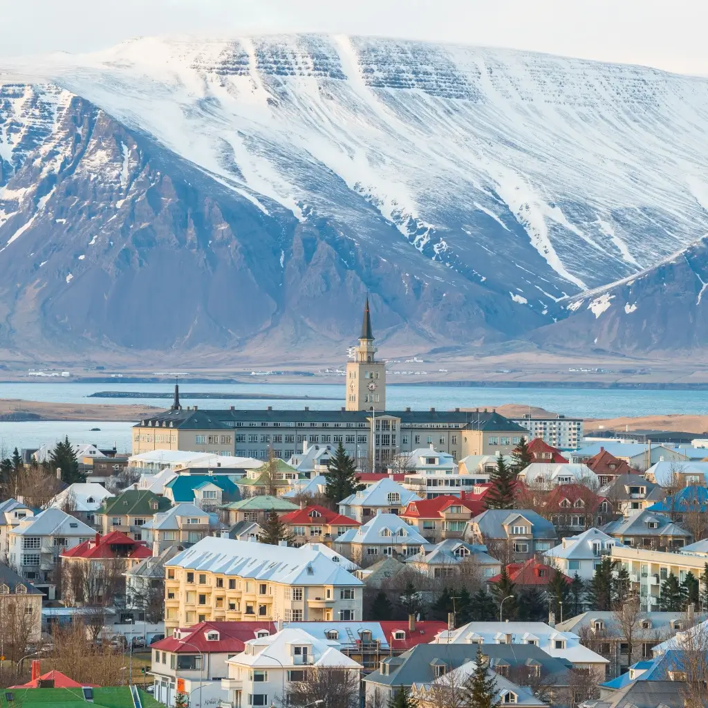 Scenic view of colorful rooftops in Reykjavik, Iceland, with a towering snow-covered mountain in the background.