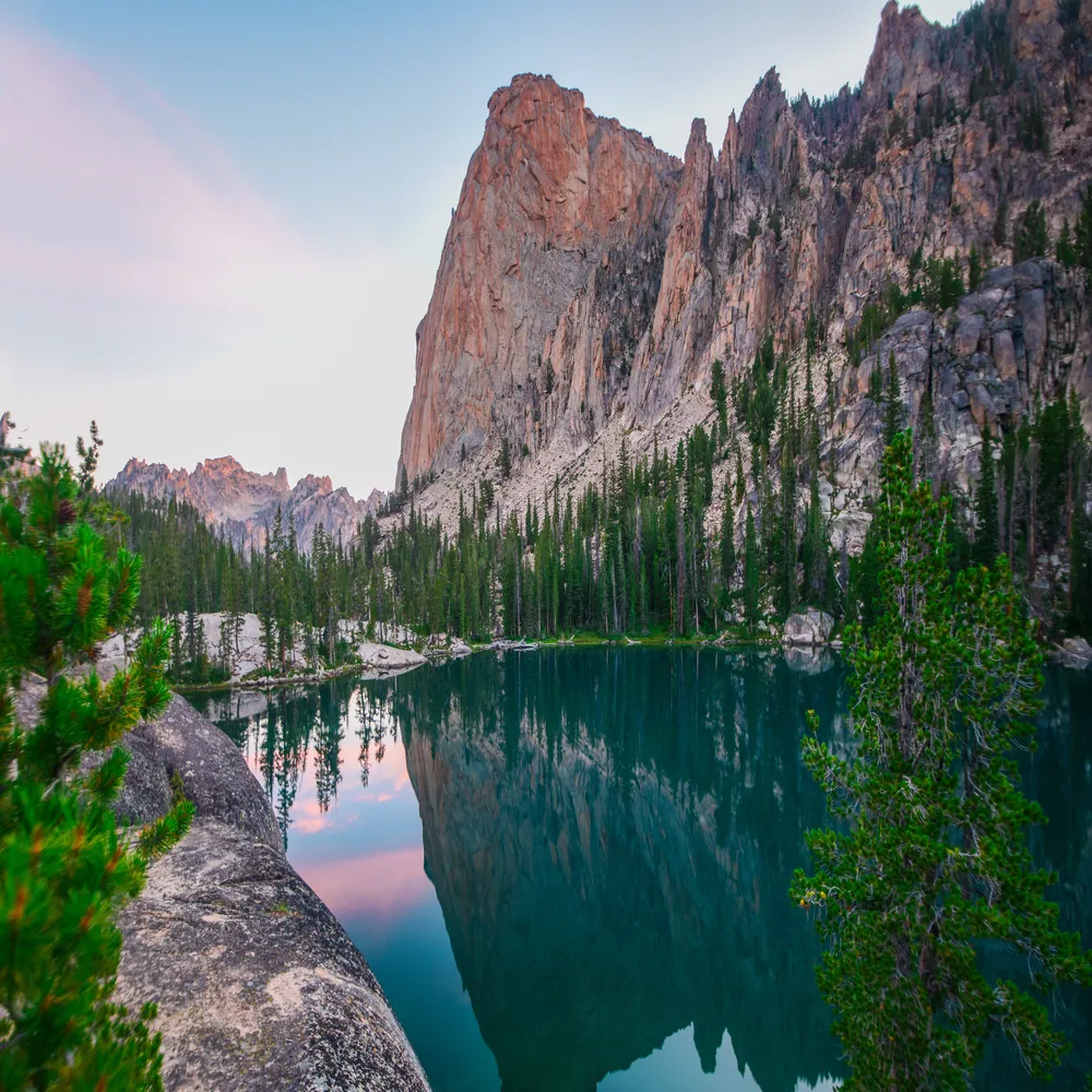 Serene landscape featuring still blue water reflecting the sky, surrounded by rugged mountain peaks and pristine nature.