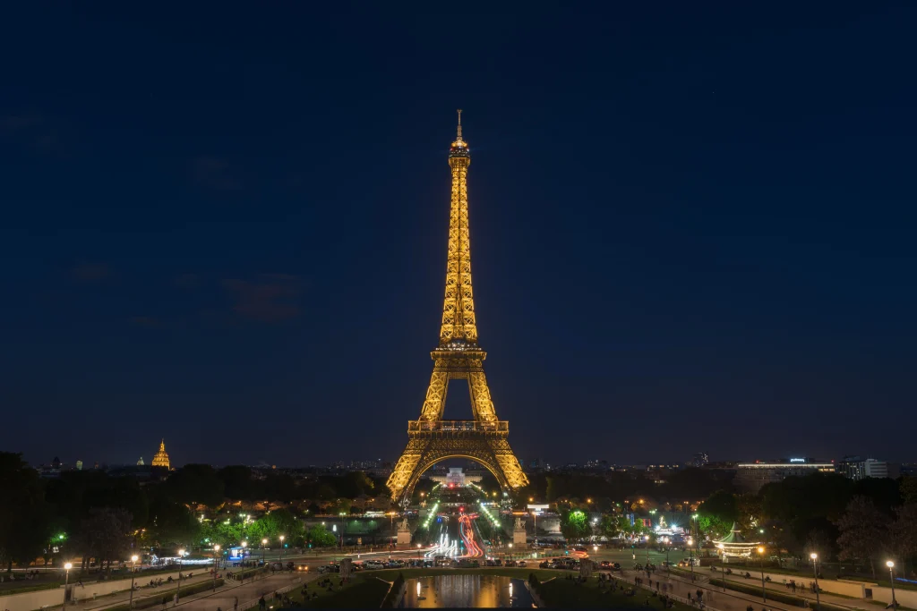 The illuminated Eiffel Tower standing against a dark blue night sky above the Paris cityscape.