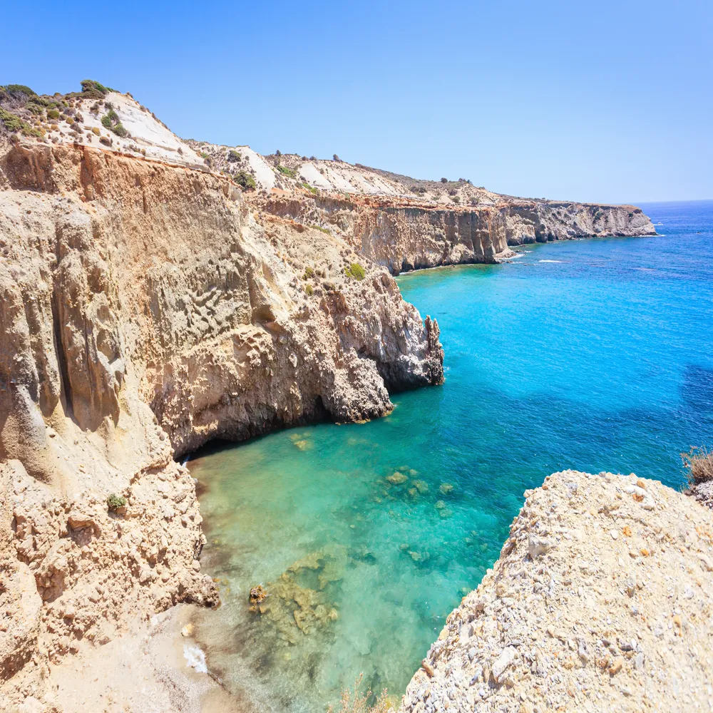 Stunning view of Tsigrado beach on Milos Island in Greece, featuring crystal clear turquoise water and secluded sandy shores surrounded by dramatic cliffs.